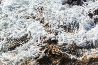 Plaj suyu karanlık kayalara çarpıyor. Korunmuş doğa.