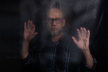 Islak bardaktan görünen, reçeteli gözlüklü kel bir adamın portresi. Siyah arkaplanda izole.