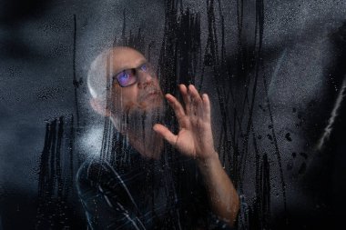 Islak bardağın arkasında gözlüklü sakallı kel bir adamın portresi elleriyle jest yapıyor. Siyah arkaplanda izole.