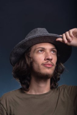 Gri şapkalı ve fotoğraf için poz veren yakışıklı bir gencin yakın plan portresi. Dumanlı siyah arkaplanda izole edilmiş.