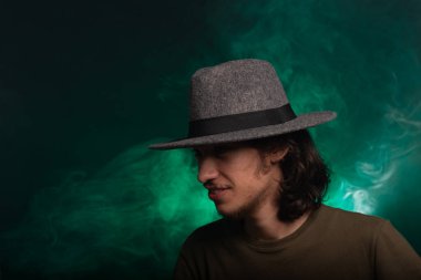 Kameraya poz veren uzun saçlı yakışıklı bir genç. Dumanlı yeşil arkaplanda izole edilmiş.