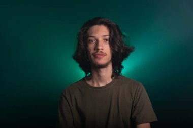 Kameraya poz veren uzun saçlı yakışıklı bir genç. Dumanlı yeşil arkaplanda izole edilmiş.