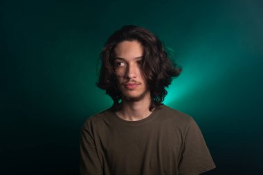 Kameraya poz veren uzun saçlı yakışıklı bir genç. Dumanlı yeşil arkaplanda izole edilmiş.