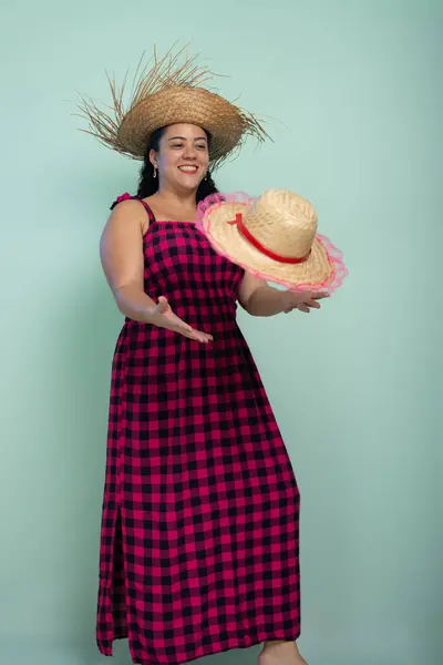 stock image Woman dressed in character for the Sao Joao festival wearing a straw hat posing for a photo and holding another hat. Braided hair and cheerful. Isolated on light background.