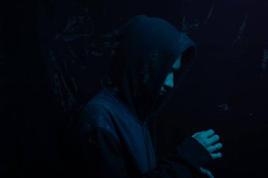 Gri kazak giyen genç adam yüzünü gizliyor. Stüdyo portresi. Mavi arkaplanda izole.