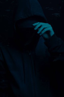 Gri kazak giyen genç adam yüzünü gizliyor. Stüdyo portresi. Mavi arkaplanda izole.