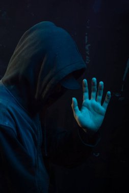 Tişörtlü gizemli genç adam kameraya avucunu gösteriyor. Yüzü gizli. Stüdyo portresi. Mavi arkaplanda izole.