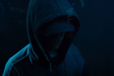 Islak camın arkasında sweatshirt giyen gizemli bir adamın portresi. Yüzü gizli. Stüdyo portresi. Mavi arkaplanda izole.
