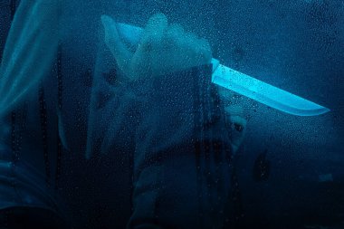 Islak camların arkasında elinde bıçak tutan gizemli bir adamın portresi. Yüzü gizli. Stüdyo portresi. Mavi arkaplanda izole.