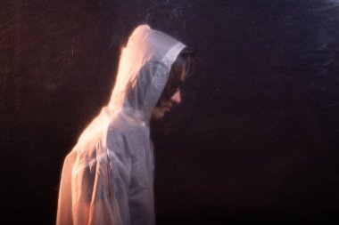 Camların arkasında şeffaf plastik yağmurluk giyen genç bir adam. Yüzü gizli. Stüdyo portresi. Koyu arkaplanda izole.