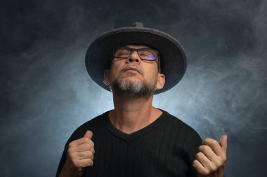 Sakallı, güneş gözlüklü ve fotoğraf için poz veren bir adamın portresi. Dumanlı arkaplana karşı.