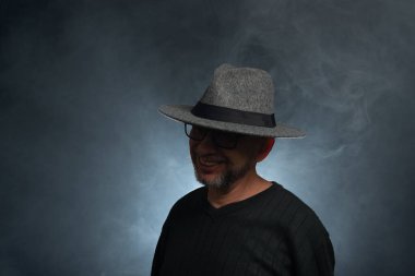 Sakallı, güneş gözlüklü ve fotoğraf için poz veren bir adamın portresi. Dumanlı arkaplana karşı.