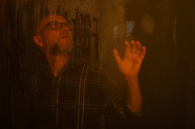 Islak sarı camlara dokunan, reçeteli gözlüklü kel bir adam. Koyu arkaplanda izole.