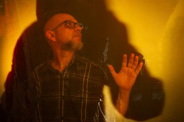 Islak sarı camlara dokunan, reçeteli gözlüklü kel bir adam. Koyu arkaplanda izole.