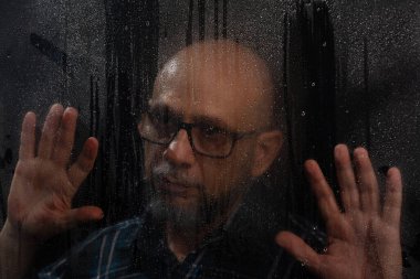 Islak cama dokunan, reçeteli gözlüklü kel adamın yakın plan portresi. Siyah arkaplanda izole.