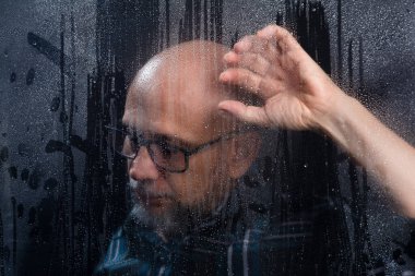 Islak camların arkasına dokunan, reçeteli gözlüklü kel sakallı adamın yakın plan portresi endişe verici ifadeler sergiliyor. Siyah arkaplanda izole.