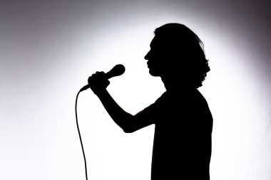 Genç şarkıcının silueti mikrofonu tutuyor ve duygu dolu bir şekilde şarkı söylüyor. Beyaz arkaplanda izole.