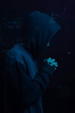 Gri kazak giyen genç adam yüzünü gizliyor. Stüdyo portresi. Mavi arkaplanda izole.