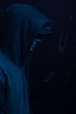 Gri kazak giyen genç adam yüzünü gizliyor. Stüdyo portresi. Mavi arkaplanda izole.