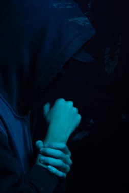 Gri kazak giyen genç adam yüzünü gizliyor. Stüdyo portresi. Mavi arkaplanda izole.