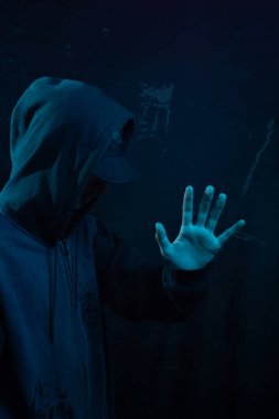 Tişörtlü gizemli genç adam kameraya avucunu gösteriyor. Yüzü gizli. Stüdyo portresi. Mavi arkaplanda izole.