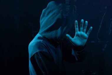 Tişörtlü gizemli genç adam kameraya avucunu gösteriyor. Yüzü gizli. Stüdyo portresi. Mavi arkaplanda izole.