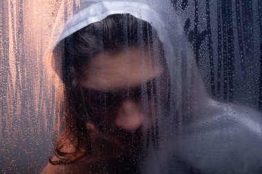 Camların arkasında şeffaf plastik yağmurluk giyen genç bir kadının yakın plan portresi. Stüdyo çekimi. Koyu arkaplanda izole.