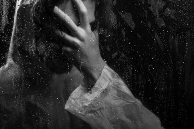 Islak camların arkasında yağmurluk giyen ve yüzünü kaplayan siyah beyaz insan portresi. Stüdyo portresi. Koyu arkaplanda izole.