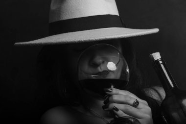 Cam bardaktan şarap içen şapkalı bir kadının siyah beyaz portresi. Stüdyo fotoğrafı.