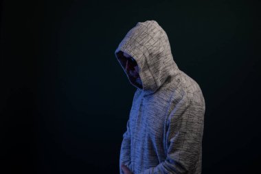 Kapüşonlu kazak giyen gizemli bir adamın portresi sessizce duruyor. Koyu arkaplanda izole.