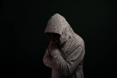 Güneş gözlüklü ve kapüşonlu kazaklı bir adam kameraya poz veriyor. Koyu arkaplanda izole.