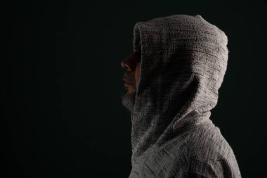 Güneş gözlüğü takan gizemli bir adam ve başını örten kapüşonlu bir kazak. Koyu arkaplanda izole.