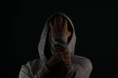 Güneş gözlüğü takan ve kafasında elleri olan kapüşonlu kazak giyen gizemli bir adamın portresini yakından çek. Koyu arkaplanda izole.