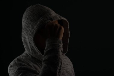 Güneş gözlüğü takan ve kafasında elleri olan kapüşonlu kazak giyen gizemli bir adamın portresini yakından çek. Koyu arkaplanda izole.