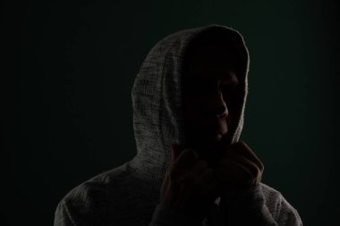 Güneş gözlüğü takan ve başını örten kapüşonlu kazak giyen gizemli adamın silueti. Koyu arkaplanda izole.