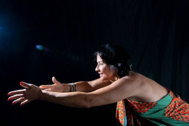 Renkli kıyafetler giyen, ışığa doğru kolları olan güzel bir kadının stüdyo portresi. Siyah arkaplanda izole.