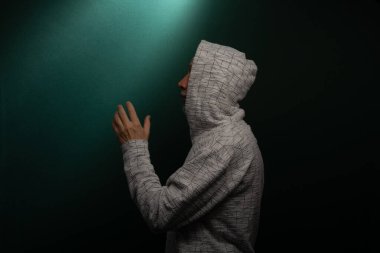 Kapüşonlu kazak giyen gizemli adam el hareketi yapıyor. Koyu arkaplanda izole.