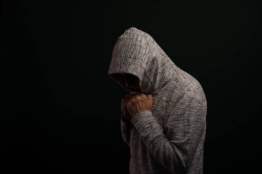 Güneş gözlüğü takan ve kapüşonlu kazak giyen hareketsiz duran el hareketleri yapan bir adamın portresi. Koyu arkaplanda izole.