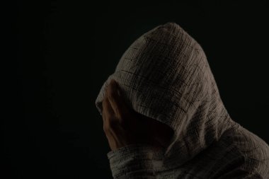 Güneş gözlüğü takan ve kafasında elleri olan kapüşonlu kazak giyen gizemli bir adamın portresini yakından çek. Koyu arkaplanda izole.