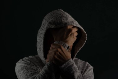 Güneş gözlüğü takan ve kafasında elleri olan kapüşonlu kazak giyen gizemli bir adamın portresini yakından çek. Koyu arkaplanda izole.