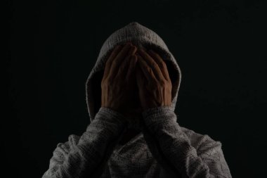 Güneş gözlüğü takan ve kafasında elleri olan kapüşonlu kazak giyen gizemli bir adamın portresini yakından çek. Koyu arkaplanda izole.