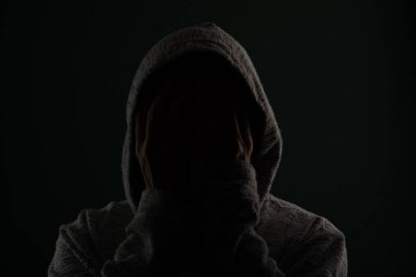 Güneş gözlüğü takan ve kafasında elleri olan kapüşonlu kazak giyen gizemli bir adamın portresini yakından çek. Koyu arkaplanda izole.