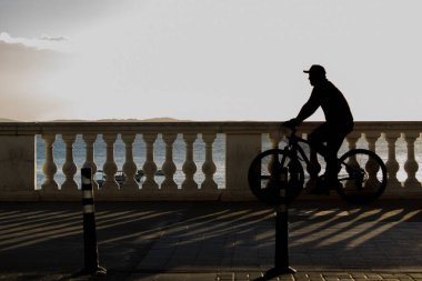 Salvador, Bahia, Brazil - June 15, 2019: An unidentified person is seen in silhouette riding a bicycle in Porto da Barra during sunset in the city of Salvador, Bahia. clipart