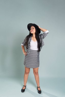 Stüdyoda poz veren genç ve güzel bir kadın. Siyah bir şapka takmış ve elinde tutuyordu. Sakin bir kadın siyah beyaz elbiseler giyiyor. Açık yeşil arkaplanda izole.