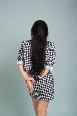 Sırtı kameraya dönük duran güzel bir kadın siyah beyaz elbiseli bir fotoğraf için sakince poz veriyor. Açık yeşil arkaplanda izole.