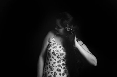 Uzun düz saçlarıyla elini gezdiren bir kadının siyah beyaz portresi. Stüdyo çekimi.