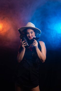 Kahverengi şapkalı, elinde şişe ve bir bardak şarap olan güzel bir kadın. Stüdyo fotoğrafı dumanlı renkli arkaplan.