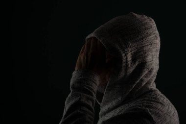 Güneş gözlüğü takan ve kafasında elleri olan kapüşonlu kazak giyen gizemli bir adamın portresini yakından çek. Koyu arkaplanda izole.