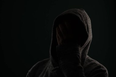 Güneş gözlüğü takan ve kafasında elleri olan kapüşonlu kazak giyen gizemli bir adamın portresini yakından çek. Koyu arkaplanda izole.