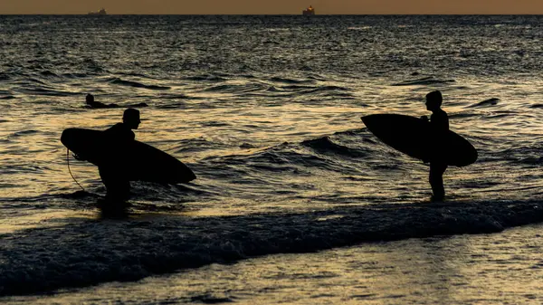 Salvador, Bahia, Brezilya - Aralık 06, 2019: Günbatımında Farol da Barra plajında iki sörfçü görüldü. Salvador, Bahia.